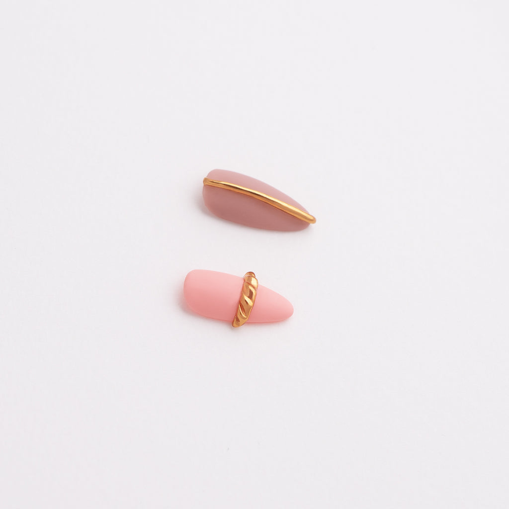 Pink press-on nail art designs with gold accents on a light gray background