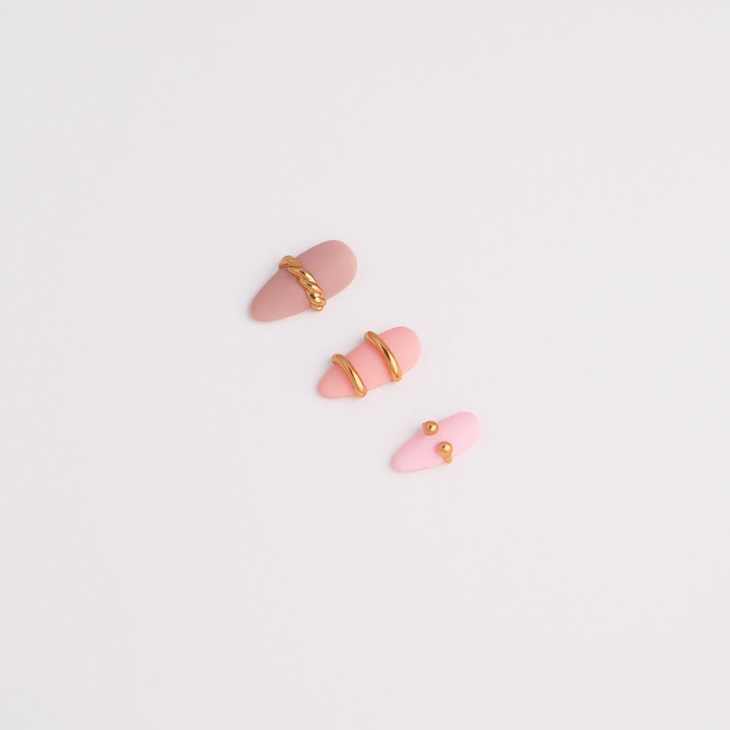 Pink press-on nail art designs with gold accents on a light gray background