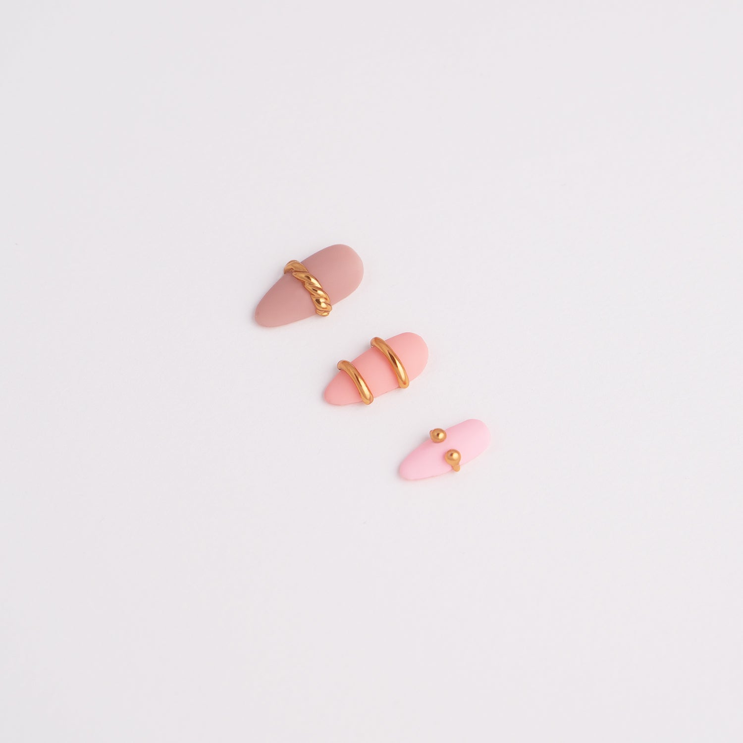 Pink press-on nail art designs with gold accents on a light gray background